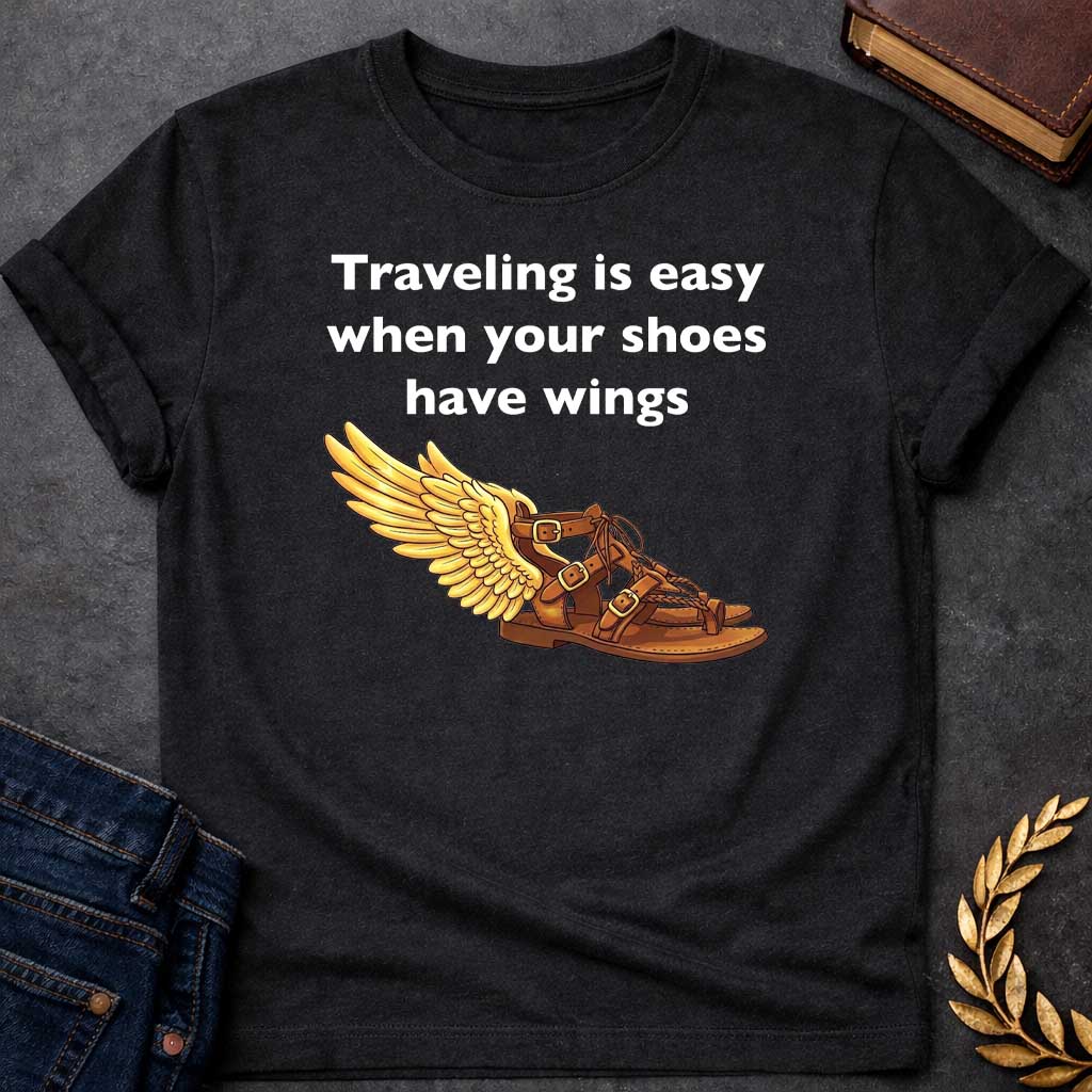 Black T-shirt graphic featuring bold white text reading "Traveling is easy when your shoes have wings" above a detailed illustration of Hermes' winged sandal, depicted as a brown leather gladiator sandal with gold buckles and braided lacing, with a large golden wing extending from the ankle — a humorous reference to the talaria, the iconic flying sandals of Hermes, the Greek Messenger God