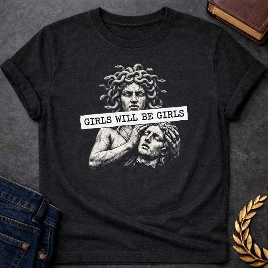 Black T-shirt graphic in black and white featuring a detailed stone sculpture-style illustration of Medusa with snake hair looming above a distressed male figure clutching his head in anguish, with a torn paper banner across the middle reading "Girls Will Be Girls" in bold typewriter font — a humorous feminist nod to the Greek mythology story of Medusa