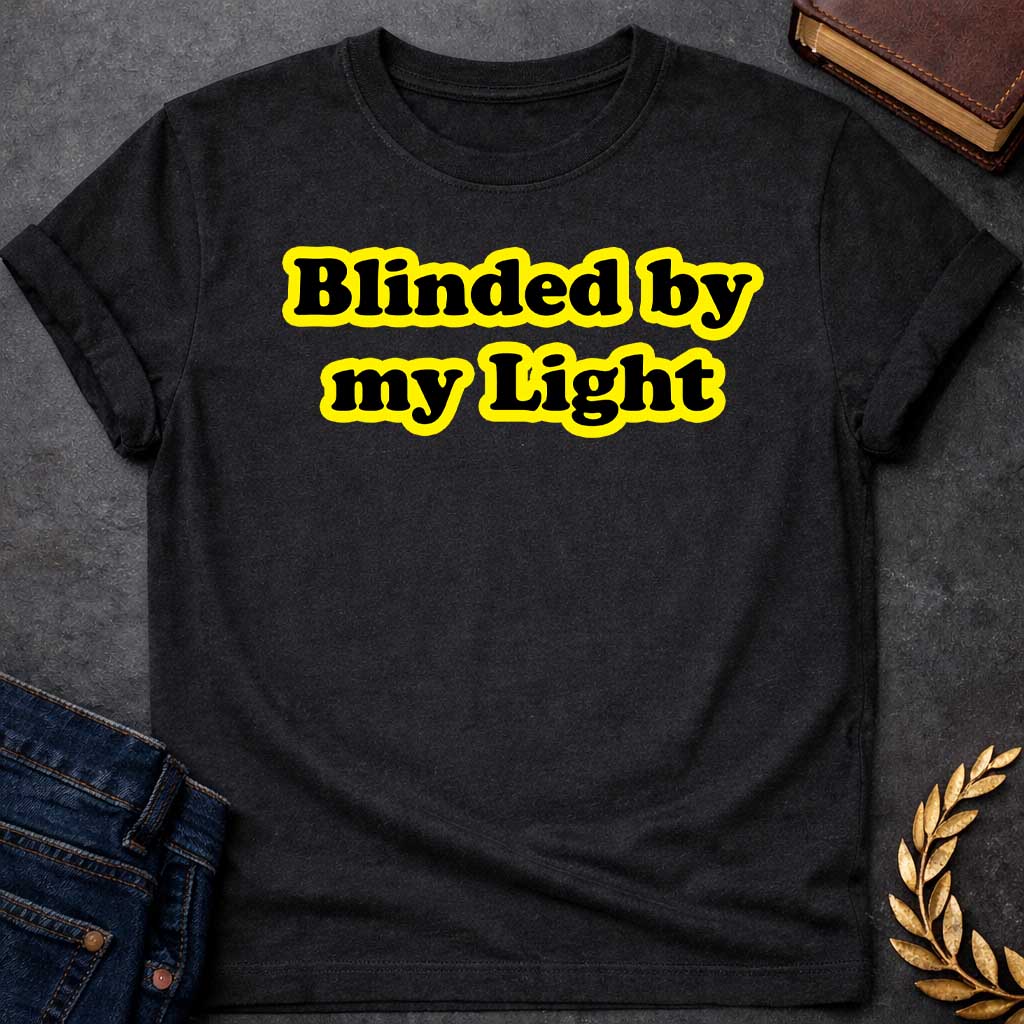 Black T-shirt Streetwear graphic design featuring the phrase "Blinded by my Light" in bold black bubble typography with a vibrant yellow glow. Retro-style aesthetic inspired by Greek mythology and Apollo, the god of light