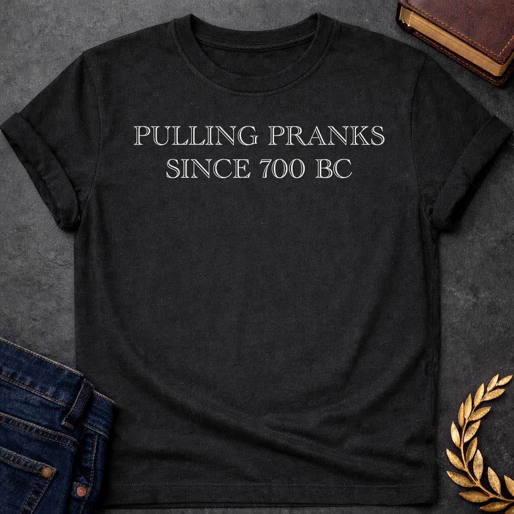 Black T-shirt graphic in white text featuring large outlined engraved-style serif text reading "Pulling Pranks Since 700 BC" — a humorous nod to Hermes, the Greek Messenger God and notorious trickster