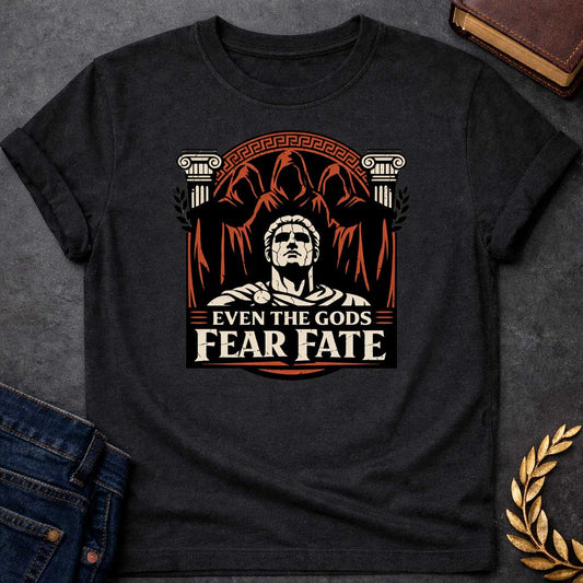Black shirt featuring a striking graphic design with a classical Greek aesthetic. In the center, a cracked marble bust of a Roman figure gazes upward, flanked by two Ionic columns. Looming behind the statue are three shadowy, hooded figures representing the Fates. The scene is enclosed in a circular Greek key border. The color palette is a bold trio of cream, burnt orange, and black. Below the art, the text reads "EVEN THE GODS" in a clean serif font and "FEAR FATE" in large, distressed block letters