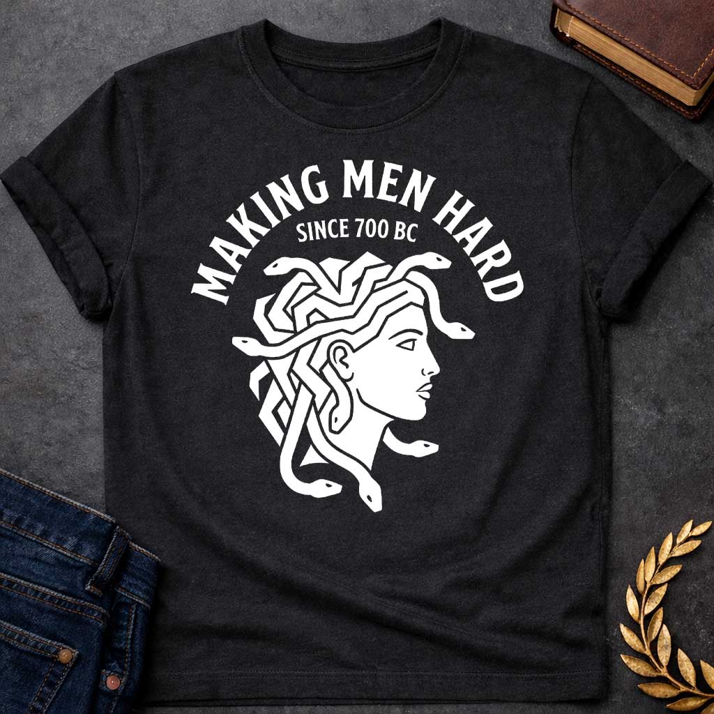 Black T-shirt graphic white featuring a bold flat graphic side-profile illustration of Medusa with snake hair, in a minimalist ancient Greek coin or seal style. Bold arched text above reads "Making Men Hard" with smaller text below it reading "Since 700 BC" — a witty double entendre referencing Medusa's mythological power to turn men to stone