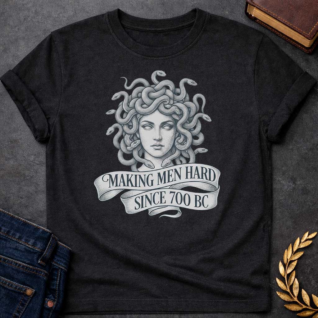 Black T-shirt graphic in grey and white featuring a highly detailed fine-line tattoo-style front-facing portrait of Medusa with numerous coiling snakes for hair, rendered in intricate stippling and engraving technique, with a flowing ribbon banner below reading "Making Men Hard Since 700 BC" — a witty double entendre referencing Medusa's mythological power to turn men to stone