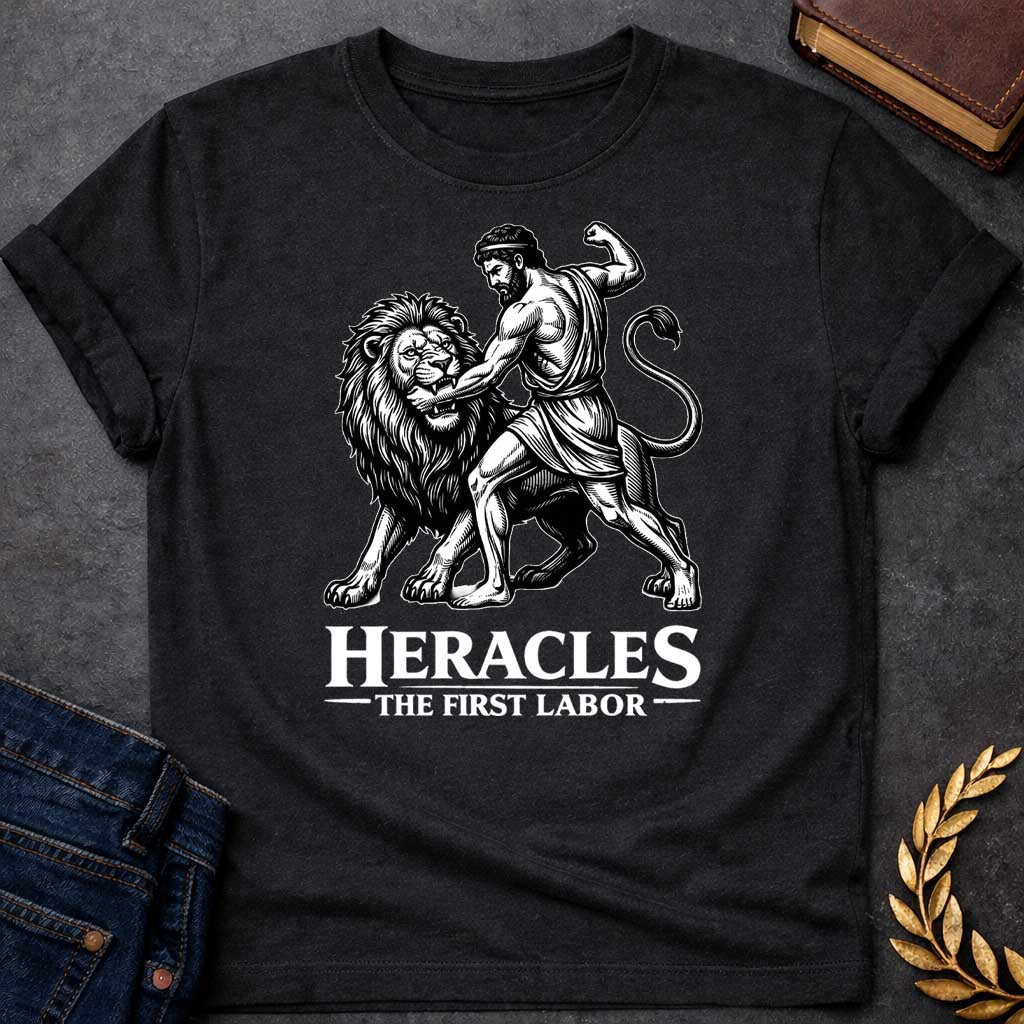 Black T-shirt. The illustration features a woodcut-style depiction of the Greek hero Heracles wrestling the Nemean lion. Below the artwork, the text reads in white "HERACLES" in a large, distressed serif font, followed by the smaller subtitle "THE FIRST LABOR,"