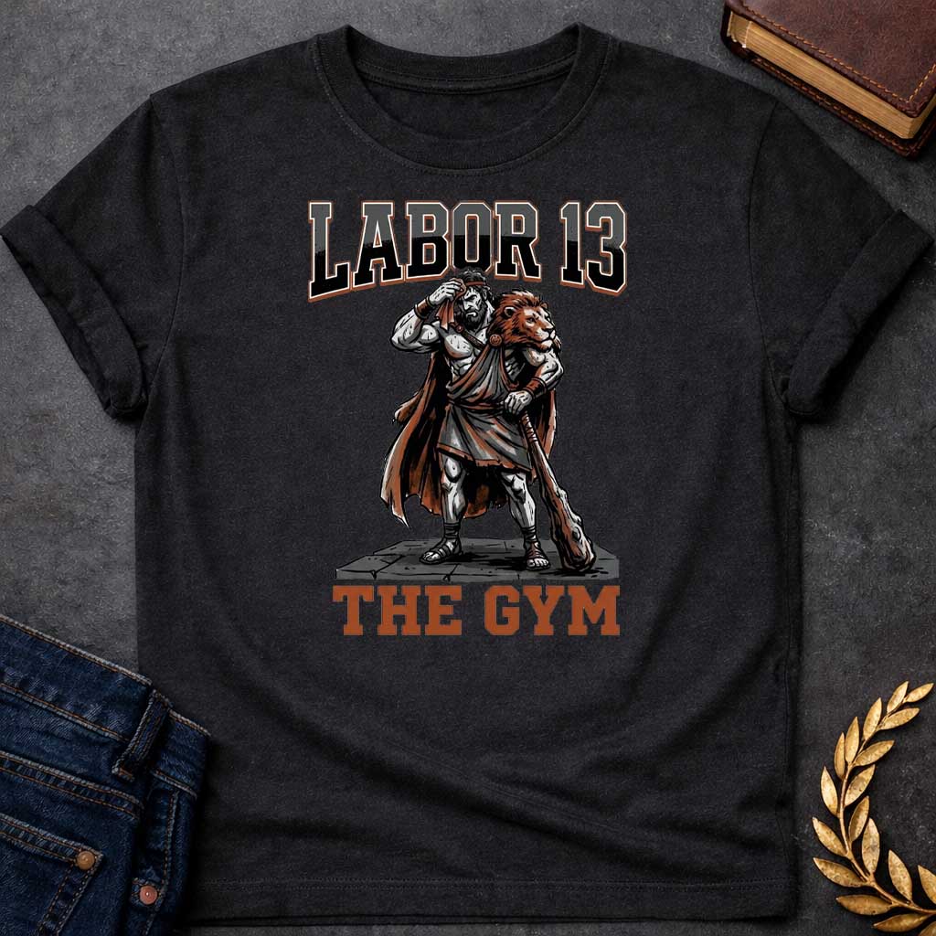 Black T-shirt featuring a sweat-drenched, muscular figure resembling Heracles, wearing a lion-skin cloak and holding a large wooden club. He stands on a stone platform while wiping his brow with a towel. The text "LABOR 13" is printed in large, bold, block letters across the top, and "THE GYM" is in a matching style at the bottom