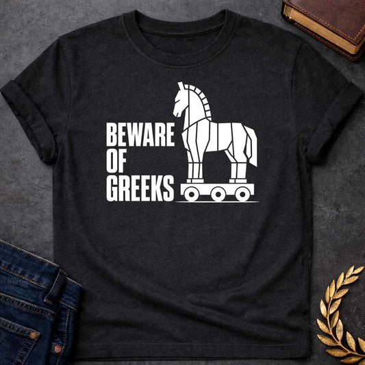 Black T-shirt with a graphic in white featuring bold condensed sans-serif text reading "Beware of Greeks" alongside a flat geometric white silhouette illustration of the Trojan Horse mounted on a wheeled platform — a humorous reference to the Greek legend of the Trojan War