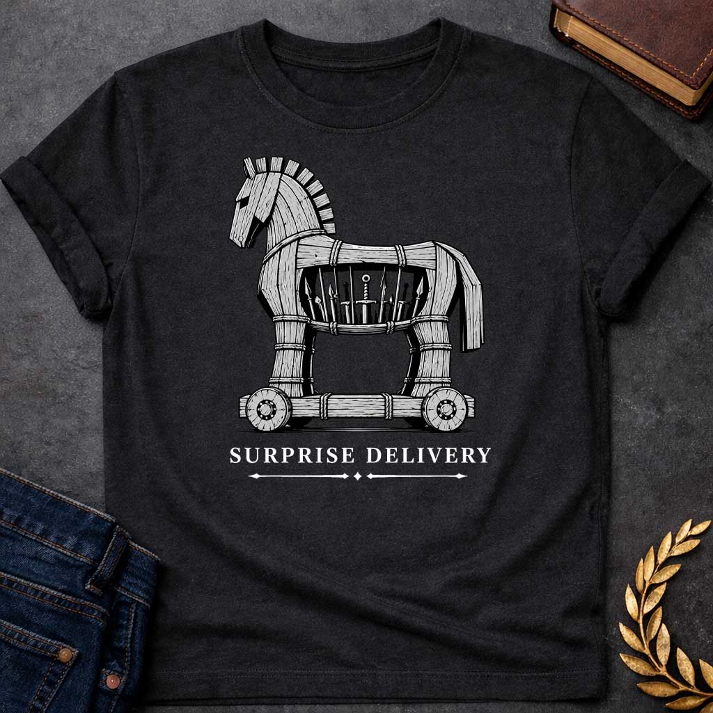 Black T-shirt with a graphic in black and white featuring a highly detailed realistic ink illustration of the Trojan Horse constructed from weathered wood planks bound with rope on a wheeled platform, with spears and a sword visibly hidden inside its hollow body. Elegant spaced serif text below with decorative arrow dividers reads "Surprise Delivery" — a humorous reference to the Greek legend of the Trojan War