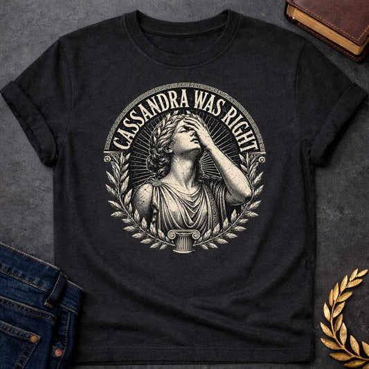 Black T-shirt with a classical engraving-style illustration of Cassandra, the Trojan prophetess, looking upward with one hand raised to her forehead in anguish. She wears flowing Greek robes with decorative brooch and Greek key pattern trim. Surrounded by laurel wreaths and flanked by Ionic columns. Radiating lines create a dramatic halo effect. Text 'CASSANDRA WAS RIGHT' curves along the top within a Greek key border. References the tragic myth of Cassandra, cursed to see the future but never be believed.