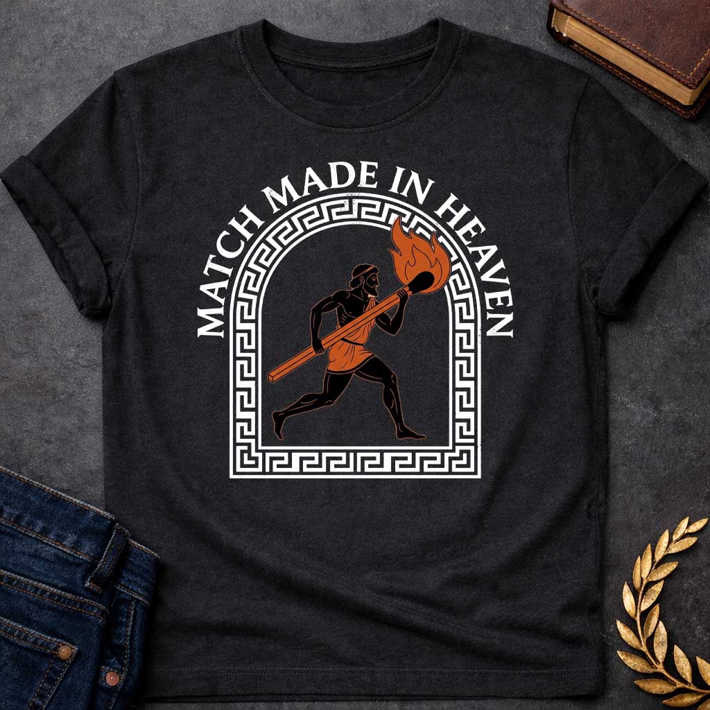 Black T-shirt with A graphic in an ancient Greek Black-Figure pottery style featuring Prometheus running while carrying a massive, burning match stick. He is depicted in black silhouette with terracotta-orange details on his tunic and the flame. The figure is framed by a white Greek key meander arch. Above the design, the pun "MATCH MADE IN HEAVEN" is written in an arched, bold white serif font.