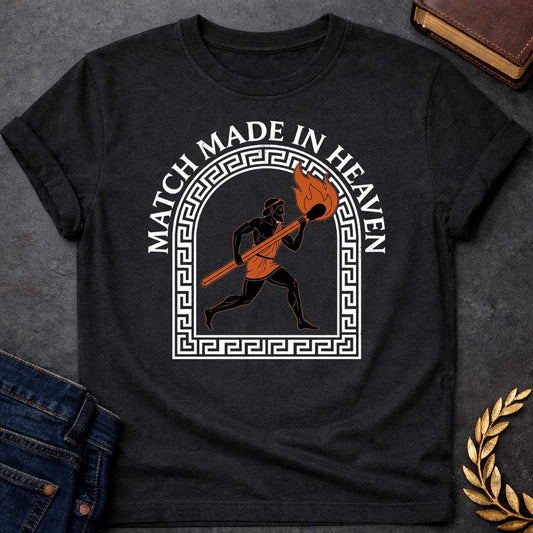 Black T-shirt with A graphic in an ancient Greek Black-Figure pottery style featuring Prometheus running while carrying a massive, burning match stick. He is depicted in black silhouette with terracotta-orange details on his tunic and the flame. The figure is framed by a white Greek key meander arch. Above the design, the pun "MATCH MADE IN HEAVEN" is written in an arched, bold white serif font.