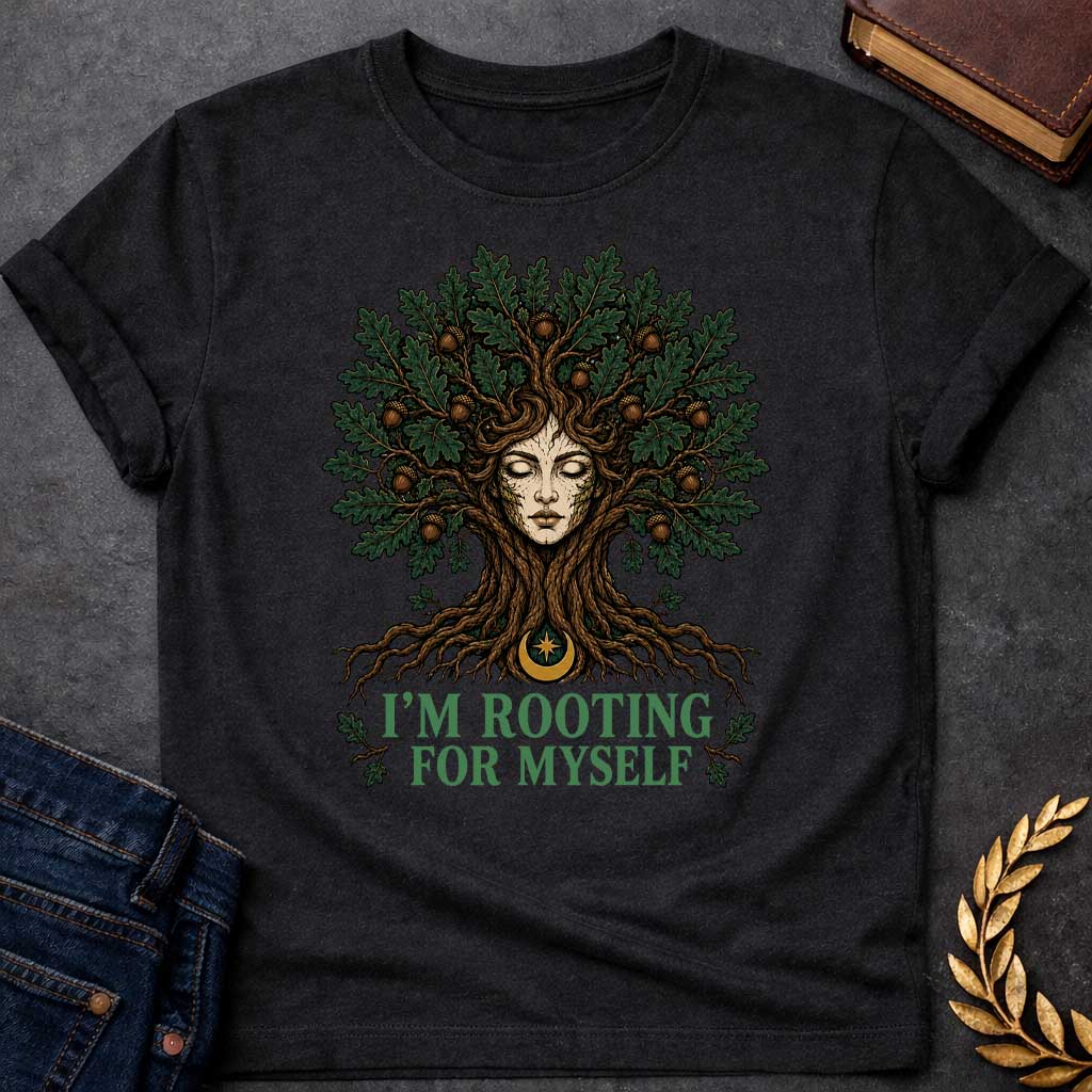 Black T-shirt with a cottagecore-style graphic featuring a detailed illustration of an oak tree dryad or nature spirit. Her serene, closed-eyed face forms the center of the tree trunk, with gnarled roots expanding below and a massive canopy of dark green oak leaves and brown acorns spreading above. Underneath the roots, a pun-based tagline reads "I'M ROOTING FOR MYSELF" in a bold, clean green serif font.