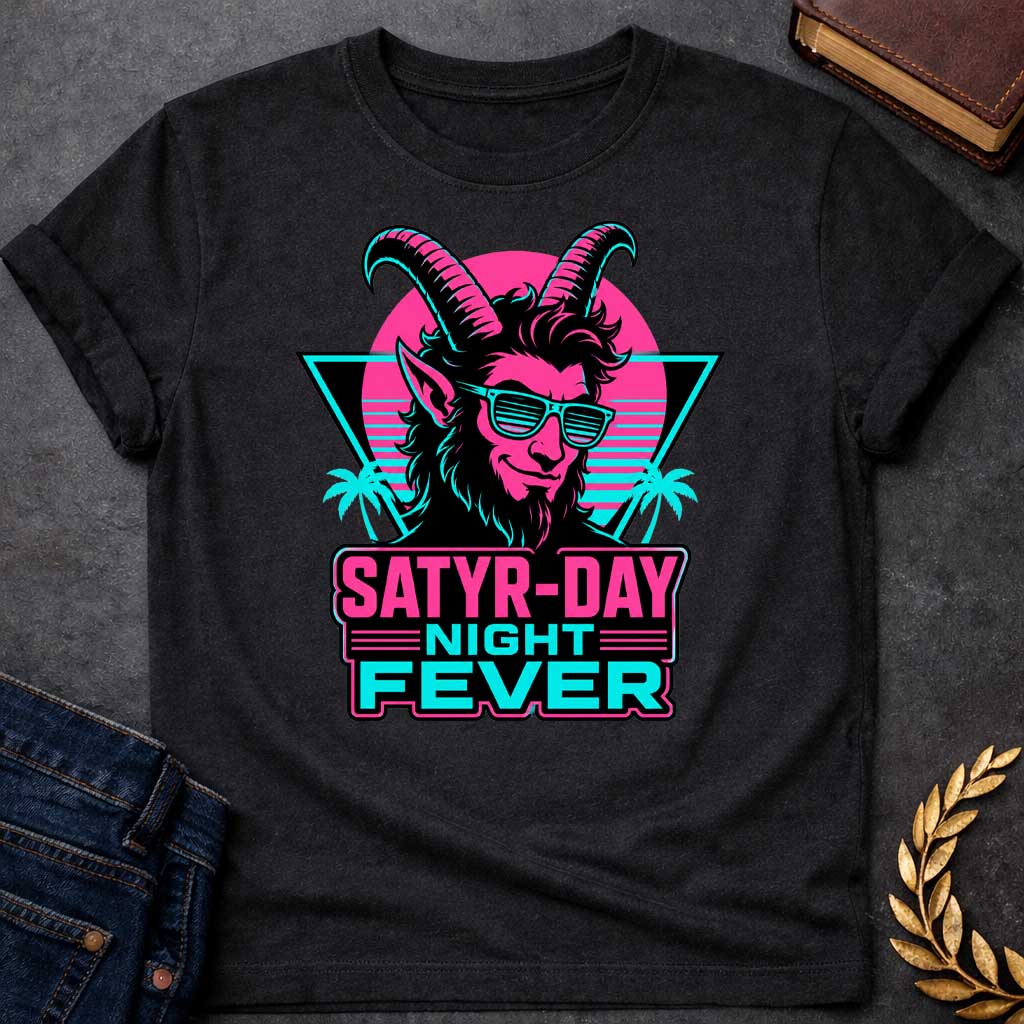 Black T-shirt with a vibrant 1980s synthwave-style graphic for "satry-day night fever.jpg". It features a cool satyr with large horns, a smirk, and cyan shutter shades, illuminated in neon pink and black. The background shows a retrowave sunset grid, a black triangle, and palm trees. Below, the punny title "SATYR-DAY NIGHT FEVER" is displayed in bold neon pink and cyan block lettering against a dark badge
