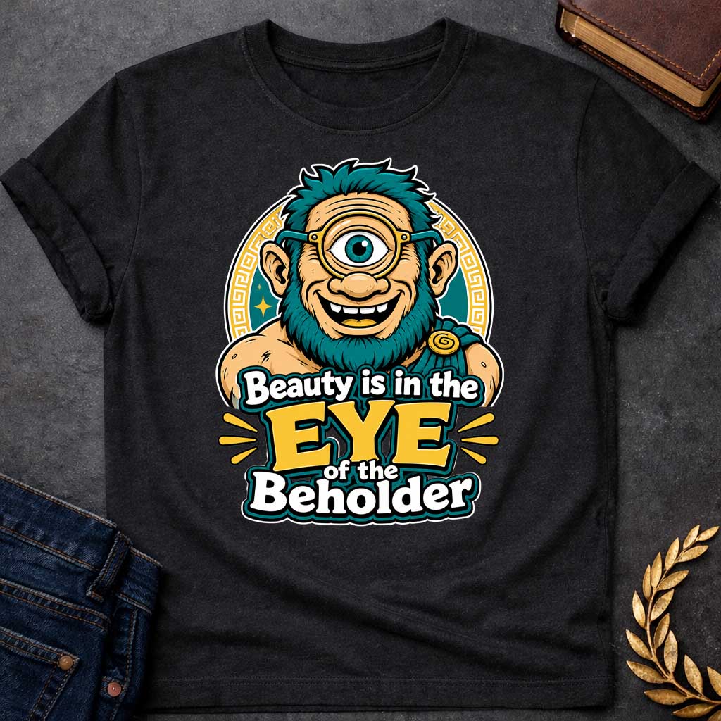 Black T-shirt with a Humorous graphic design featuring a cheerful creature with exaggerated facial features inspired by Argus Panoptes, the many-eyed giant from Greek mythology. A large teal eye with a golden monocle dominates the character's smiling face. Teal spiky hair and beard contrast with peachy skin tones. Greek key pattern borders frame the design in gold and teal. Text reads 'Beauty is in the Eye of the Beholder' in bold white and yellow lettering. Playful visual pun celebrating perspective.