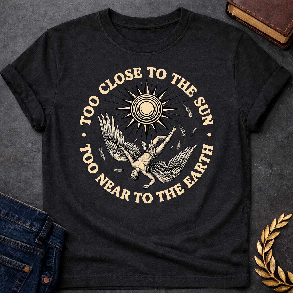 Black t-shirt with a vintage engraved-style illustration. A winged figure of Icarus plummets downward upside down as loose feathers drift through the air beneath a large, radiating sun emblem. Encircling the detailed central artwork, bold black serif text reads "TOO CLOSE TO THE SUN" along the top arch and "TOO NEAR TO THE EARTH" along the bottom curve.