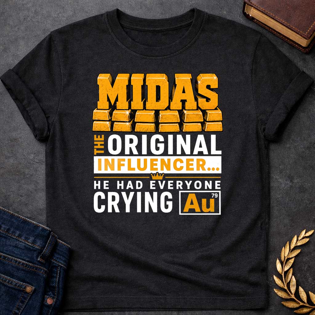 Black t-shirt with A Bold typographic Greek mythology design featuring stacked gold bar lettering spelling "MIDAS" above the phrase "The Original Influencer... He Had Everyone Crying Au." The design uses distressed black and metallic gold typography with a small crown icon and a gold-themed chemical element "Au" symbol, creating a humorous King Midas pun in a vintage-inspired graphic style.
