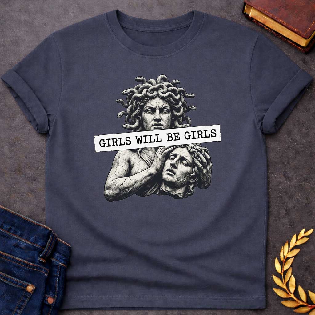 Dark Heather T-shirt graphic in black and white featuring a detailed stone sculpture-style illustration of Medusa with snake hair looming above a distressed male figure clutching his head in anguish, with a torn paper banner across the middle reading "Girls Will Be Girls" in bold typewriter font — a humorous feminist nod to the Greek mythology story of Medusa