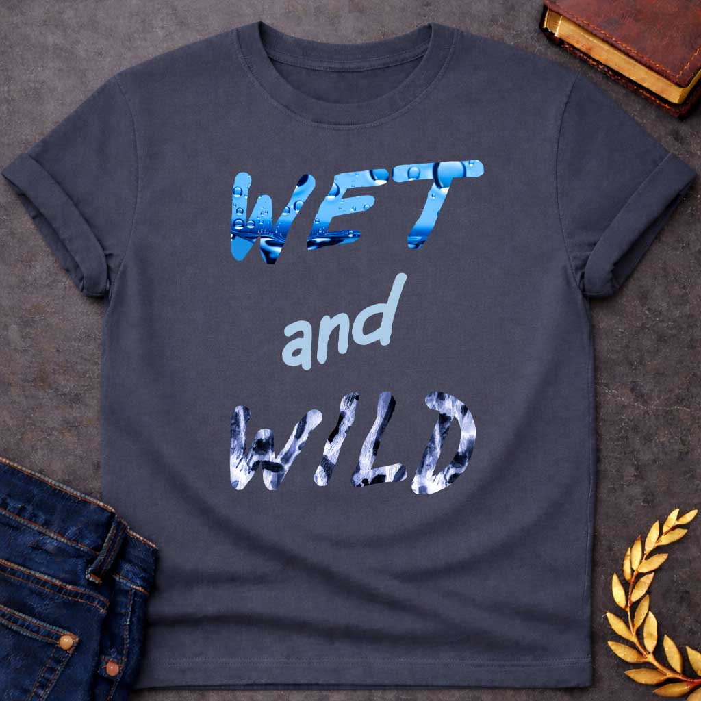 Dark Heather T-Shirt with a graphic design featuring the phrase "WET and WILD" in three stacked rows. The word "WET" is at the top in a large, bold, sans-serif font. The letters are filled with a high-definition image of bright blue water and splashing droplets. The word "and" is in the center in a smaller, lowercase, light-blue cursive-style font. The word "WILD" is at the bottom in the same large, bold font as "WET," but the letters are filled with a black-and-white leopard or cheetah print pattern