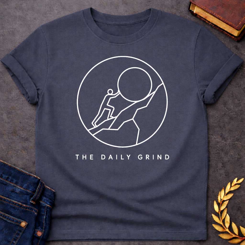 Dark Heather T-Shirt with a minimalist white graphic design.  Inside a thin circle is a simple line-art illustration of a stick figure pushing a large boulder up a steep hill, representing the myth of Sisyphus. Below the circle, the text reads "THE DAILY GRIND" in a clean, sans-serif font.