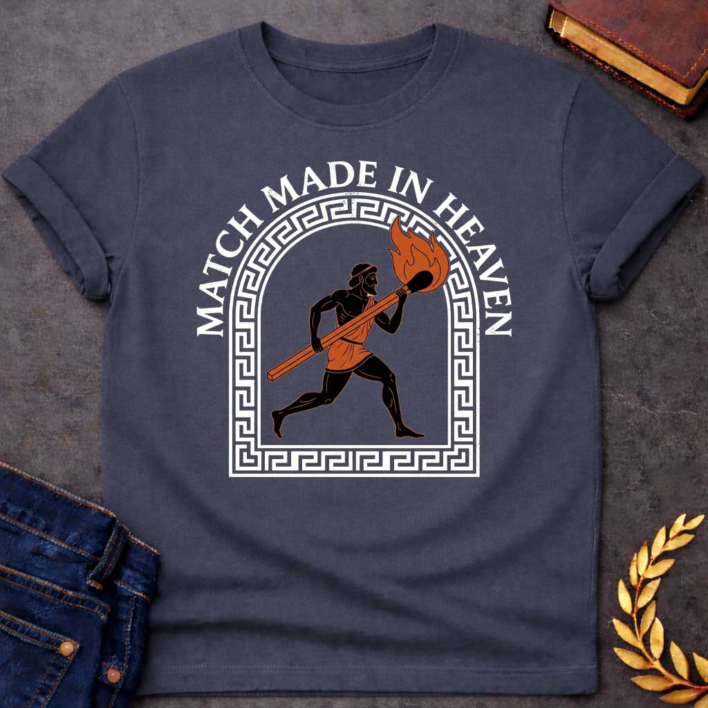 Dark Heather T-shirt with A graphic in an ancient Greek Black-Figure pottery style featuring Prometheus running while carrying a massive, burning match stick. He is depicted in black silhouette with terracotta-orange details on his tunic and the flame. The figure is framed by a white Greek key meander arch. Above the design, the pun "MATCH MADE IN HEAVEN" is written in an arched, bold white serif font.
