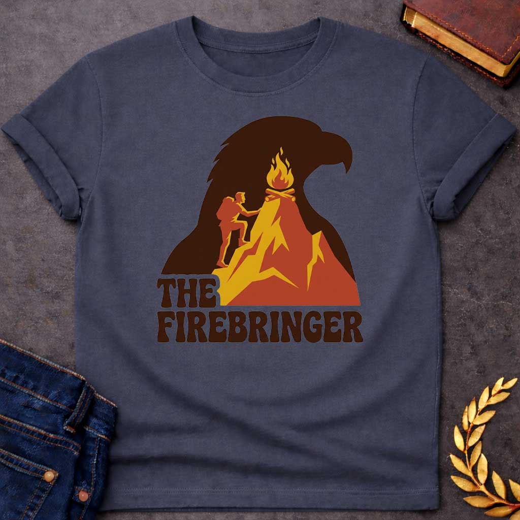Dark Heather T-shirt with a retro, outdoor-style t-shirt graphic referencing Prometheus. It features a silhouette of a hiker with a backpack climbing an orange and yellow mountain peak toward a campfire at the top. The entire mountain scene is set against a large background silhouette of an eagle's head in dark brown. Below the image, the text "THE FIREBRINGER" is written in a bold, stylized 1970s-style brown font.