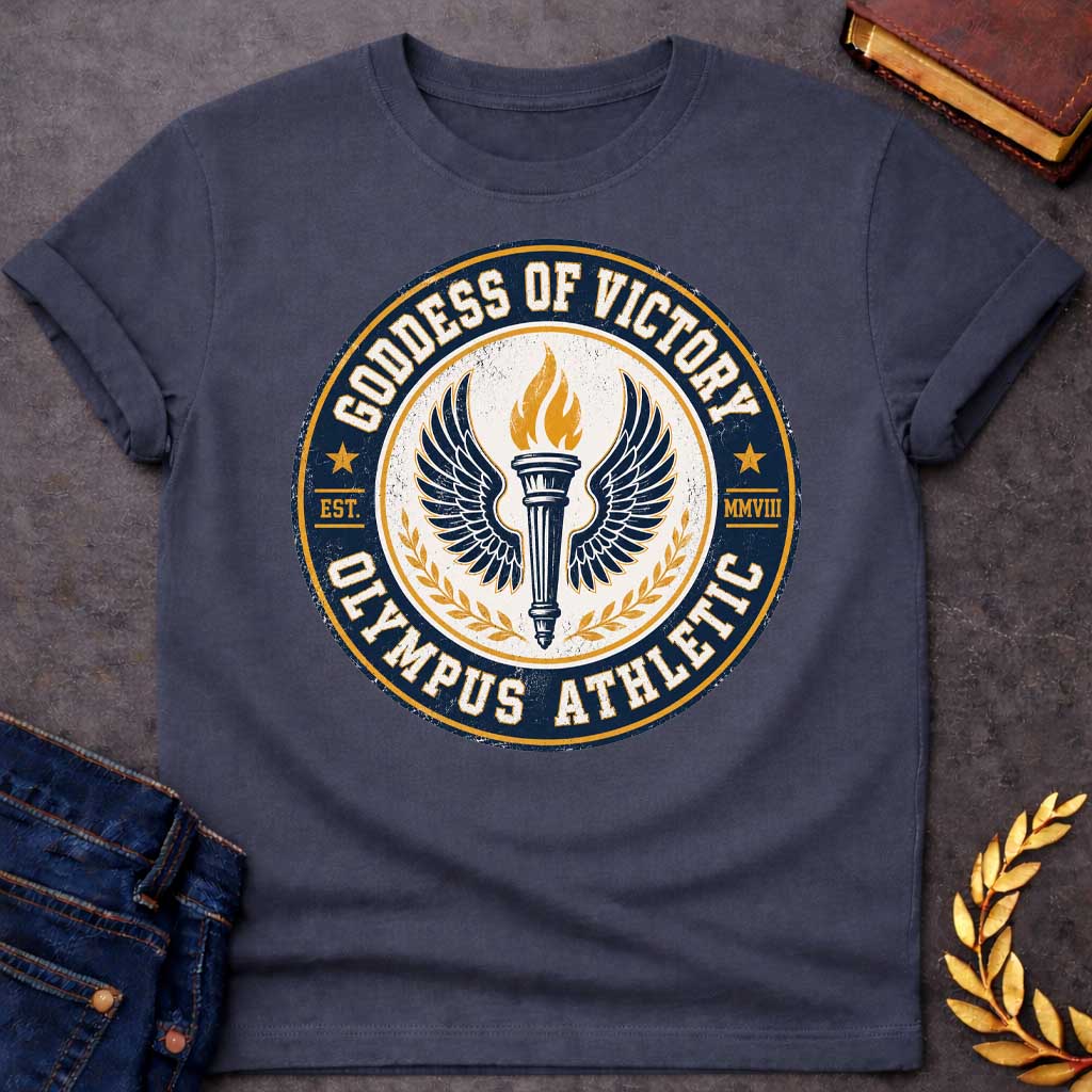 Dark Heather T-shirt with an Official athletic seal in navy blue, cream, and gold featuring a torch with large outstretched wings symbolizing Nike, the goddess of victory. Flames burn from the torch. Olive wreaths frame either side. Text reads 'GODDESS OF VICTORY' and 'OLYMPUS ATHLETIC' around the circular border with 'EST. MMVIII.' Distressed vintage texture and gold stars enhance the emblem. Celebrates athletic achievement and triumph.
