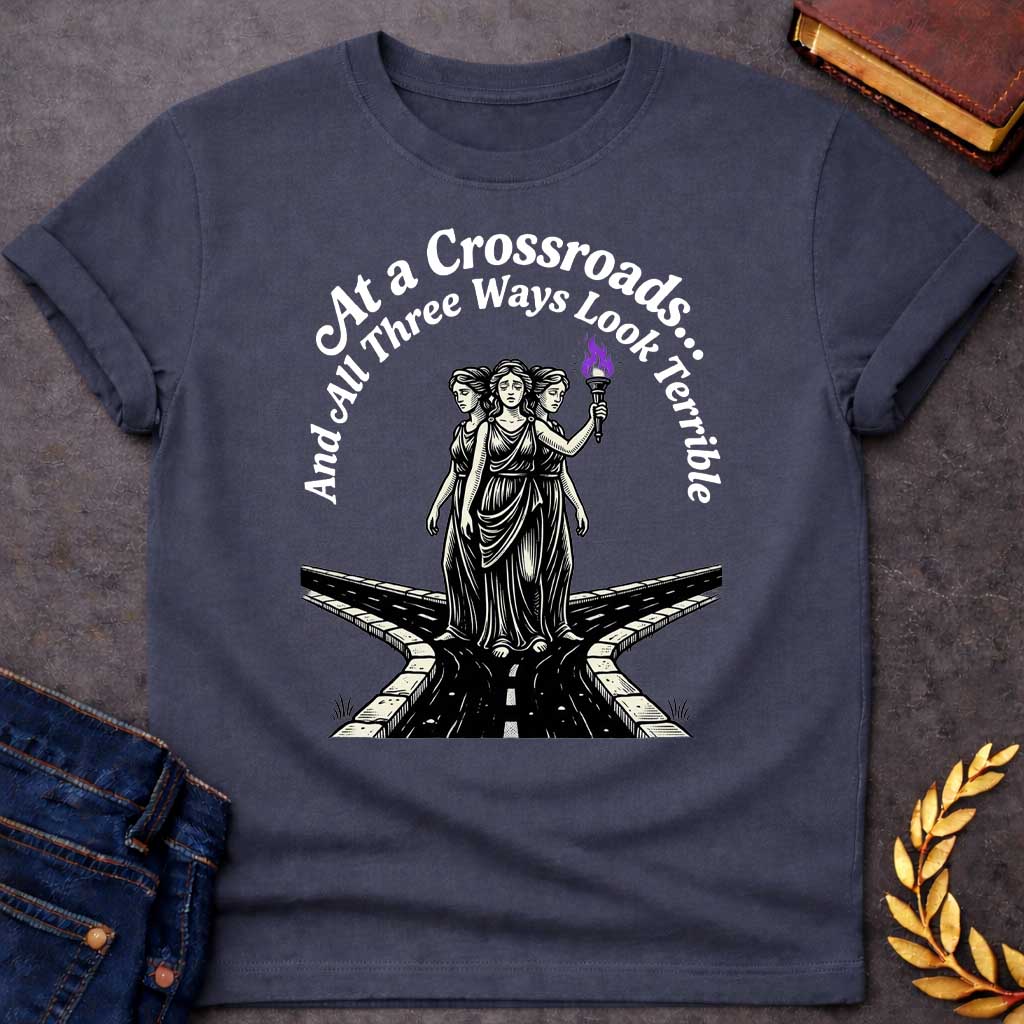 Dark Heather T-shirt with an Illustration of the Hecate at a crossroads, rendered in black and white engraving style. The figures wear flowing robes and stand together, with the center holding a flaming torch with purple flames. Text reads 'At a Crossroads: And All Three Ways Look Terrible,' humorously referencing difficult choices and Hecate’s role as goddess of the crossroads. Multiple roads branch beneath them in perspective, receding into darkness symbolizing uncertainty.
