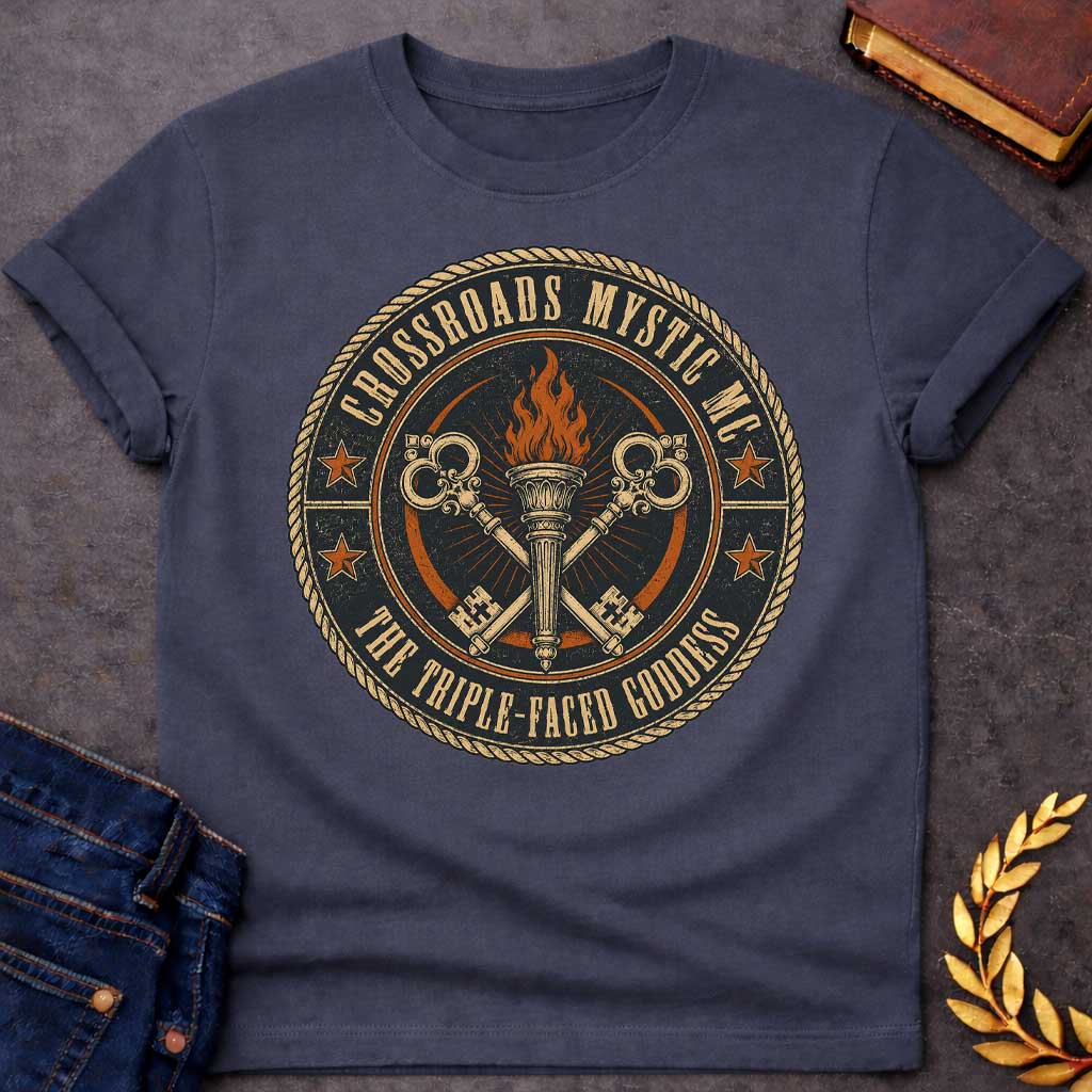 Dark Heather T-shirt with a Motorcycle club patch-style emblem in navy, gold, and orange inspired by Hecate and crossroads mythology. A central ornate torch with orange flames is flanked by two crossed serpent handles with decorative gold scrollwork. Radiating lines suggest divine power. Text reads 'Crossroads Mystic MC' and 'The Triple-Faced Goddess' around the border. Orange stars and rope border complete the official club patch look. Distressed texture adds authentic biker aesthetic.