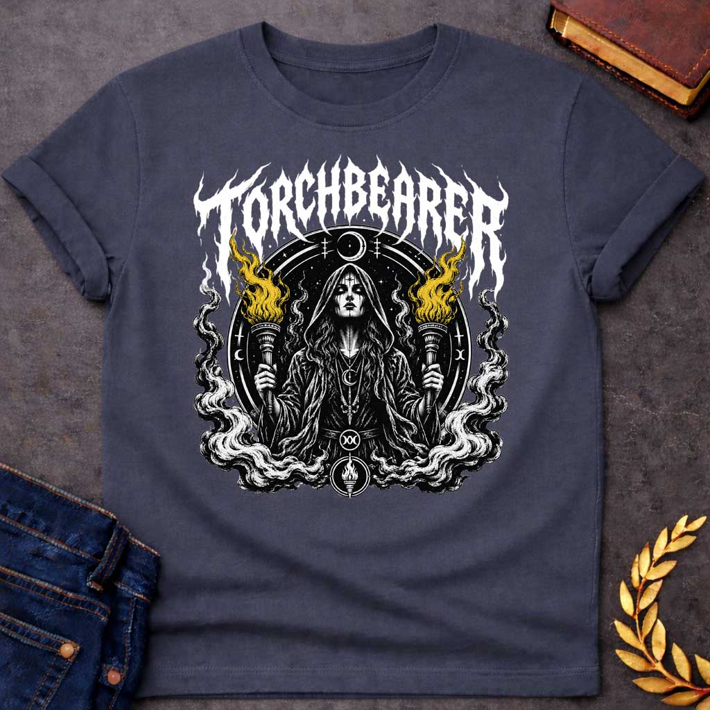 Dark Heather T-shirt with a Dark metal band aesthetic illustration titled 'Torchbearer.' Hecate holds two ornate torches with gold and black flames. She wears mystical symbols including a crescent moon necklace and a circular mandala halo with occult iconography. Swirling smoke and flame designs surround the figure in black, white, and gold. Blends heavy metal imagery with Greek mythology and mystical symbolism celebrating enlightenment, divine knowledge, and dark power.