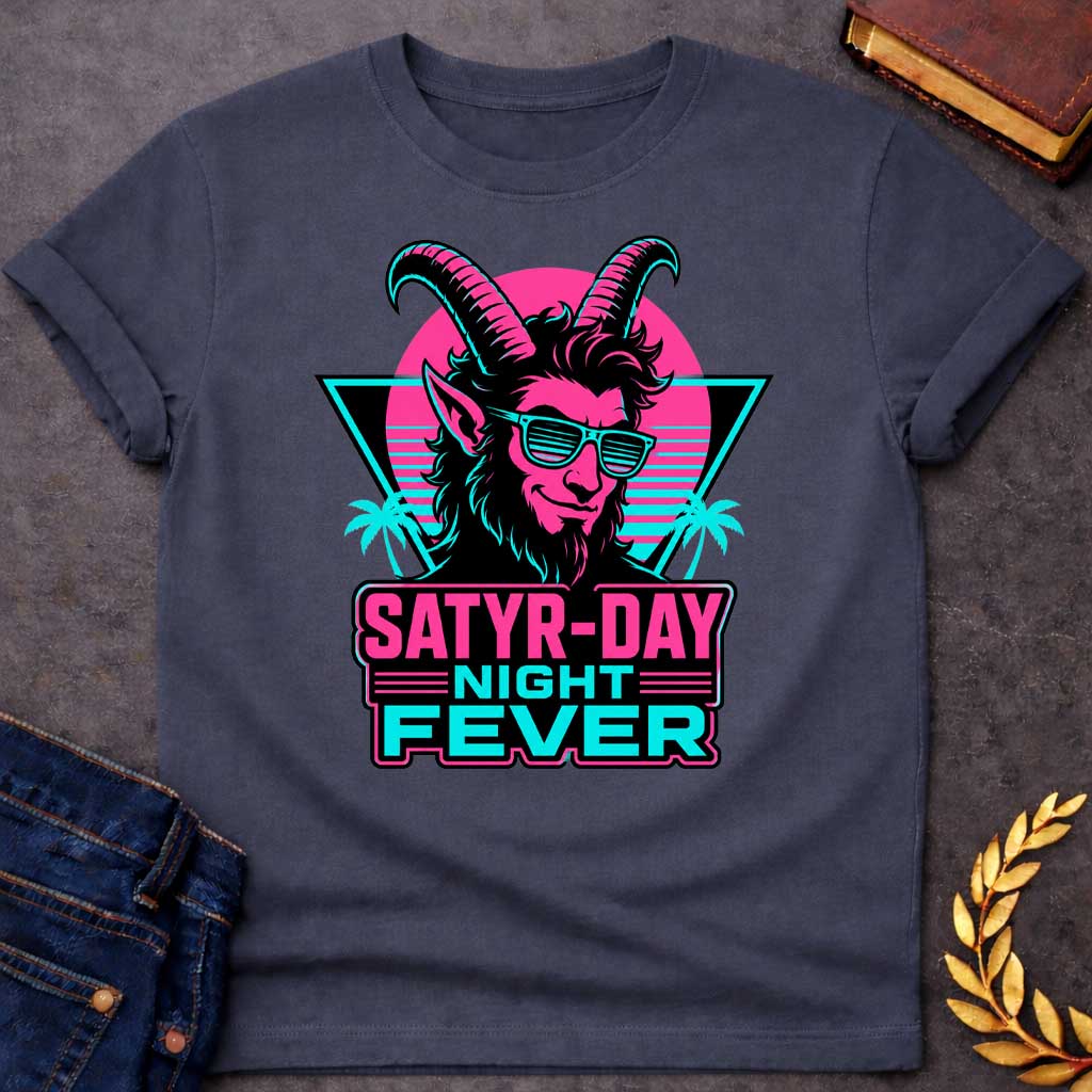 Dark Heather T-shirt with a vibrant 1980s synthwave-style graphic for "satry-day night fever.jpg". It features a cool satyr with large horns, a smirk, and cyan shutter shades, illuminated in neon pink and black. The background shows a retrowave sunset grid, a black triangle, and palm trees. Below, the punny title "SATYR-DAY NIGHT FEVER" is displayed in bold neon pink and cyan block lettering against a dark badge