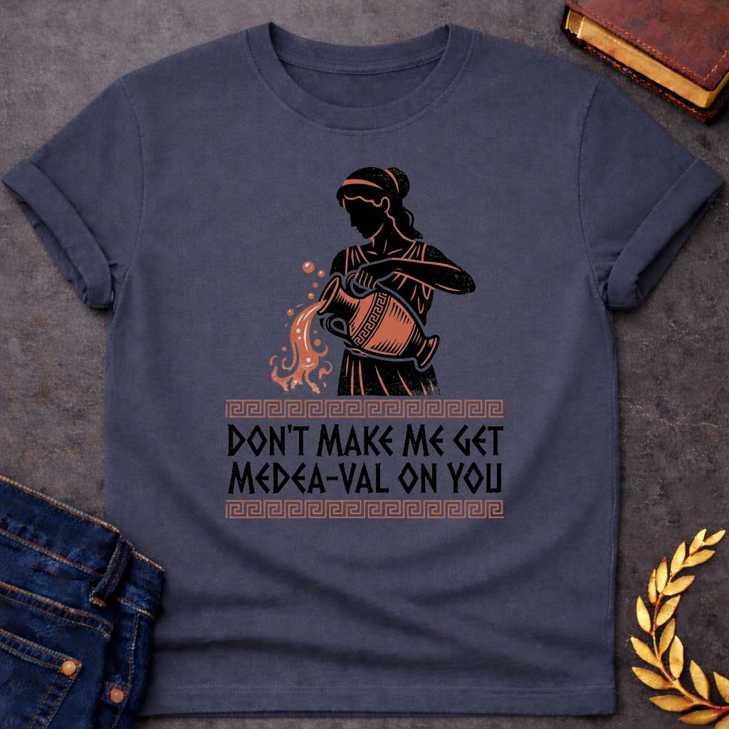Dark Heather T-shirt with A Silhouetted figure of Medea, legendary Greek sorceress, rendered in black and rust-red. She wears classical robes and headband while holding an ornate cauldron with magical flames and sparks bursting forth. Greek key pattern borders frame the design. Text reads 'Don't Make Me Get Medea-Val On You' - wordplay combining her name with modern slang. Celebrates Medea's fearsome magical and destructive powers with contemporary humor.