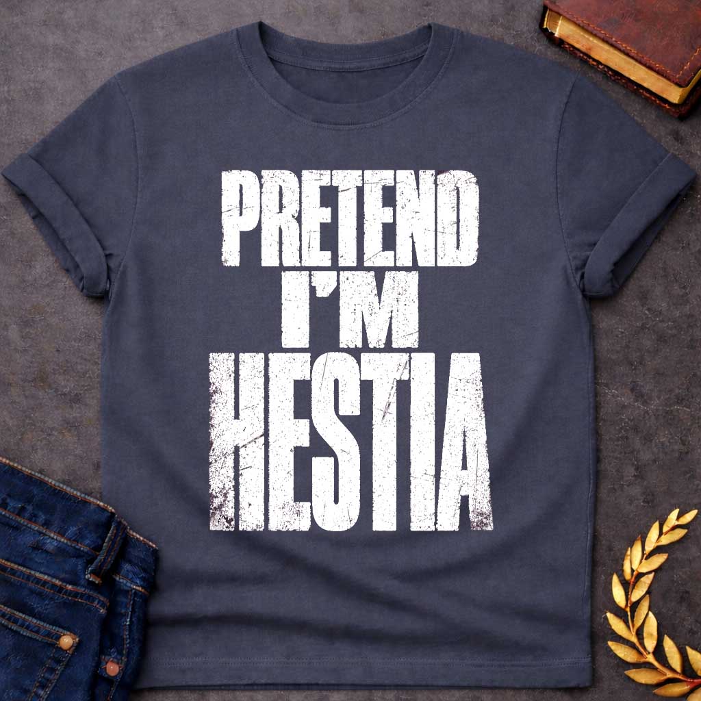 Dark Heather t-shirt with a Pretend I’m Hestia Greek mythology design featuring bold distressed white typography on a transparent background. The stacked text reads “PRETEND I’M HESTIA” in a rugged vintage block font, creating a humorous design inspired by Hestia, the Greek goddess of the hearth, home, family, and domestic life.