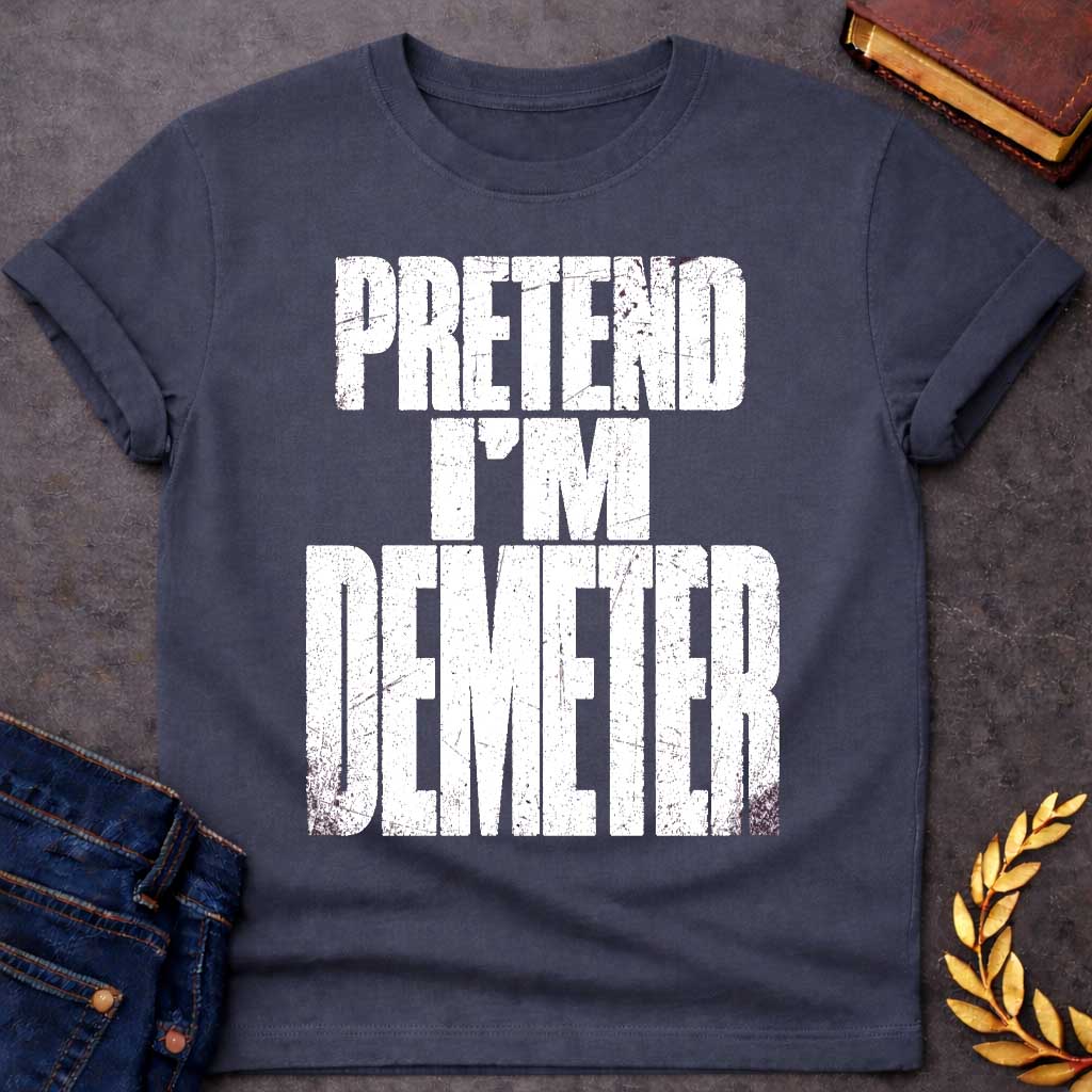 Dark Heather t-shirt with a Pretend I’m Demeter Greek mythology design featuring bold distressed white typography on a transparent background. The stacked text reads “PRETEND I’M DEMETER” in a rugged vintage block font, creating a humorous design inspired by Demeter, the Greek goddess of agriculture, harvest, grain, fertility, and the earth.