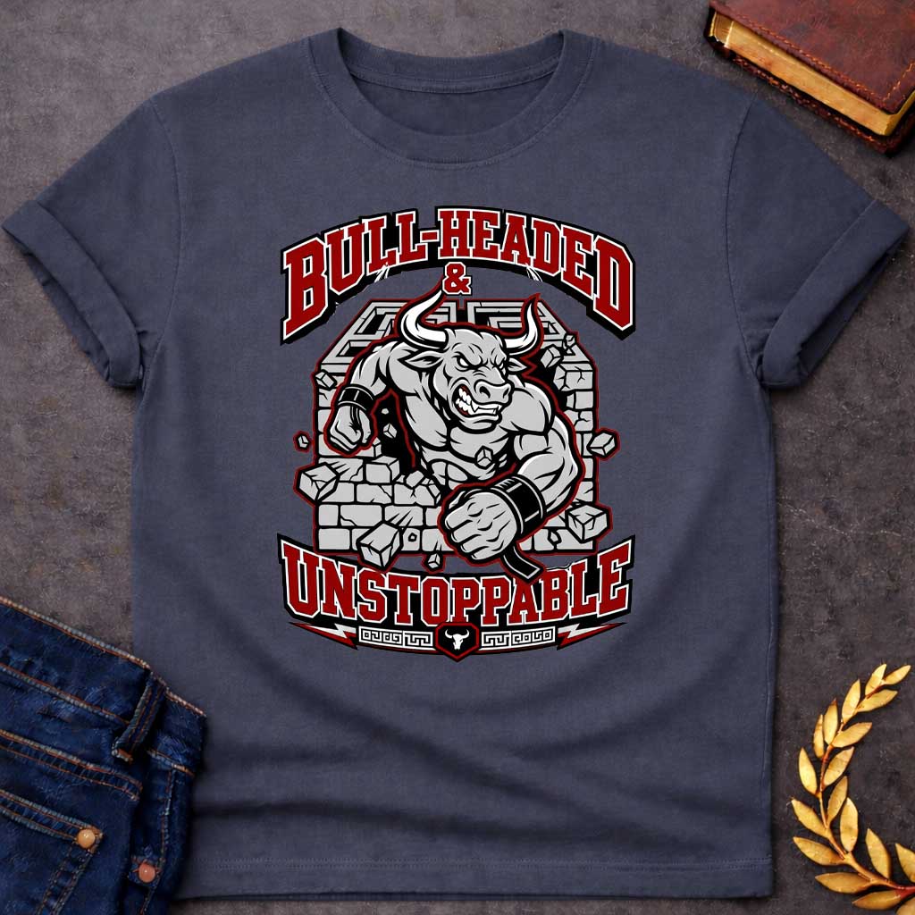 Dark Heather T-shirt with a High-impact sports design featuring a muscular Minotaur bursting through a crumbling stone wall in red, gray, and white. The aggressive bull-headed figure displays defined musculature and determination. Text reads 'Bull-Headed & Unstoppable' in bold red and black lettering. Greek key pattern and bull symbol anchor the bottom. Combines Greek mythology with modern gym and sports culture, celebrating stubborn strength and unstoppable power.