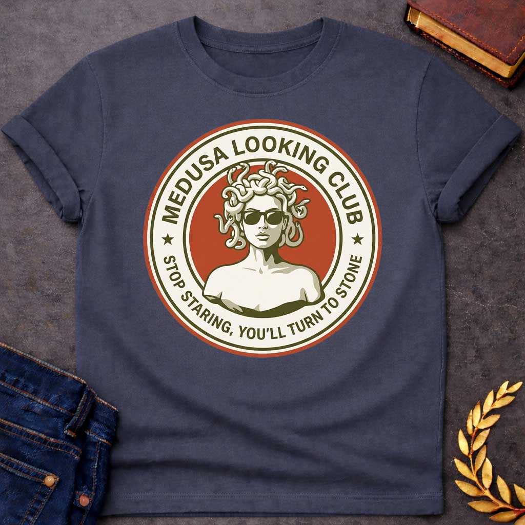 Dark Heather t-shirt in retro badge style: a cool, sunglasses-wearing Medusa with snake hair stands confidently against a burnt-orange circle. Cream and olive-green ring text reads "Medusa Looking Club" above and "Stop Staring, You'll Turn to Stone" below, with two stars flanking the design.