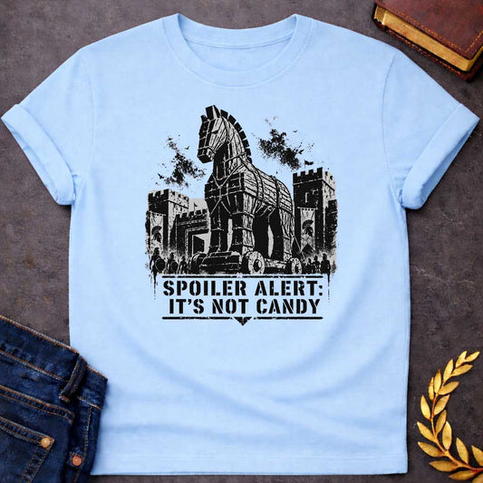Light Blue T-shirt with a graphic in black featuring a gritty detailed ink splatter-style illustration of the Trojan Horse towering over the walls of Troy, flanked by Spartan warriors with shields and spears and castle battlements with birds circling overhead. Bold military stencil text in a distressed banner below reads "Spoiler Alert: It's Not Candy" — a humorous reference to the Greek legend of the Trojan War