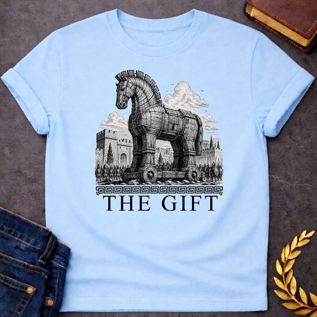 Light Blue T-shirt with a graphic in black featuring an exceptionally detailed fine-line engraving-style illustration of the Trojan Horse towering over the walls of Troy, surrounded by crowds of armored Greek soldiers with spears and shields, set against dramatic billowing clouds. A Greek meander border separates the scene from large bold classical serif text below reading "The Gift" — an ironic reference to the Greek legend of the Trojan War