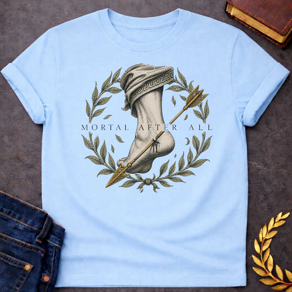 Light Blue T-Shirt with a classical engraving-style illustration depicting Achilles' fatal vulnerability. A muscular leg and foot rendered in detailed cross-hatching, draped in cloth with Greek key pattern. A golden arrow pierces the heel. Framed by a laurel wreath with olive-green leaves and falling leaves, symbolizing victory and mortality. Elegant serif text reads 'MORTAL AFTER ALL.' Muted tones of cream, grey, olive green, and gold create a somber quality reflecting Achilles' death by arrow to his only 