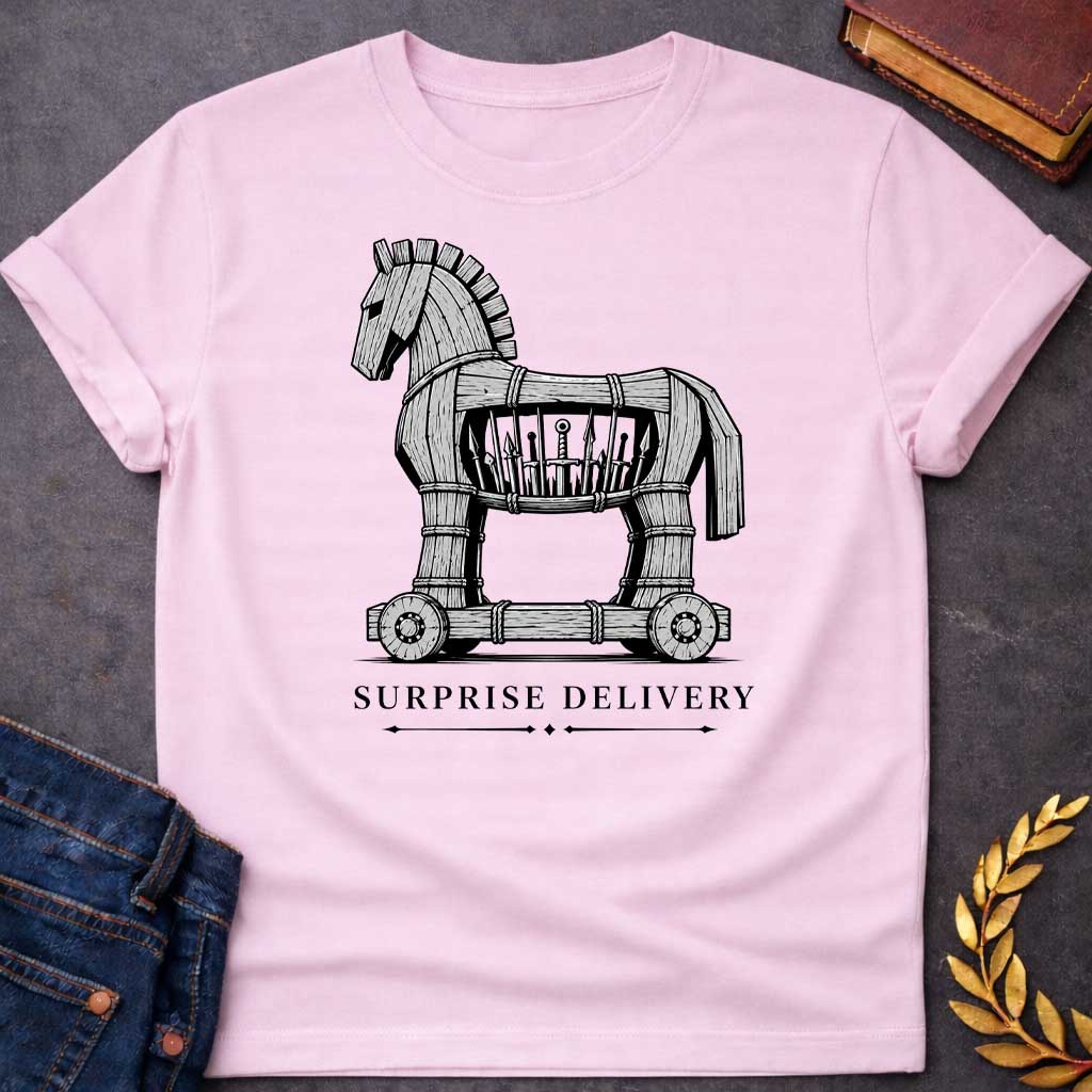 Light Pink T-shirt with a graphic in black and white featuring a highly detailed realistic ink illustration of the Trojan Horse constructed from weathered wood planks bound with rope on a wheeled platform, with spears and a sword visibly hidden inside its hollow body. Elegant spaced serif text below with decorative arrow dividers reads "Surprise Delivery" — a humorous reference to the Greek legend of the Trojan War