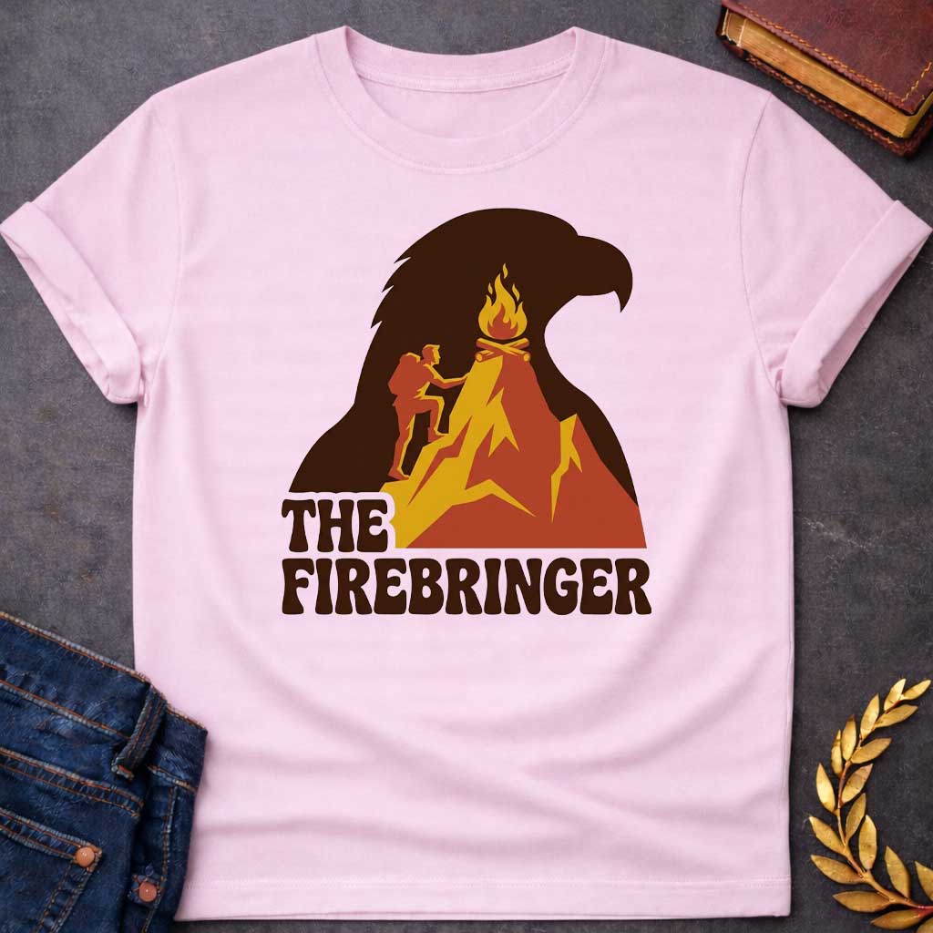 Light Pink T-shirt with a retro, outdoor-style t-shirt graphic referencing Prometheus. It features a silhouette of a hiker with a backpack climbing an orange and yellow mountain peak toward a campfire at the top. The entire mountain scene is set against a large background silhouette of an eagle's head in dark brown. Below the image, the text "THE FIREBRINGER" is written in a bold, stylized 1970s-style brown font.