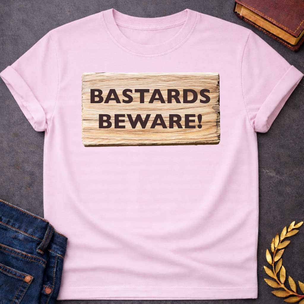 Light Pink T-shirt graphic featuring a realistic illustration of a weathered and splintered wooden plank sign with bold dark brown text reading "Bastards Beware!" in a humorous nod to Hera, the Greek Queen of the Gods, known for her jealous wrath toward Zeus's illegitimate children