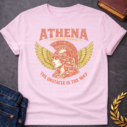 Light Pink t-shirt graphic featuring a side-profile illustration of Athena wearing a Corinthian helmet with a red plume, flanked by large golden wings. Text reads "ATHENA – Goddess of Wisdom" arched above and "The Obstacle Is the Way" curved below, in a vintage Greek mythology style with rose and gold tones