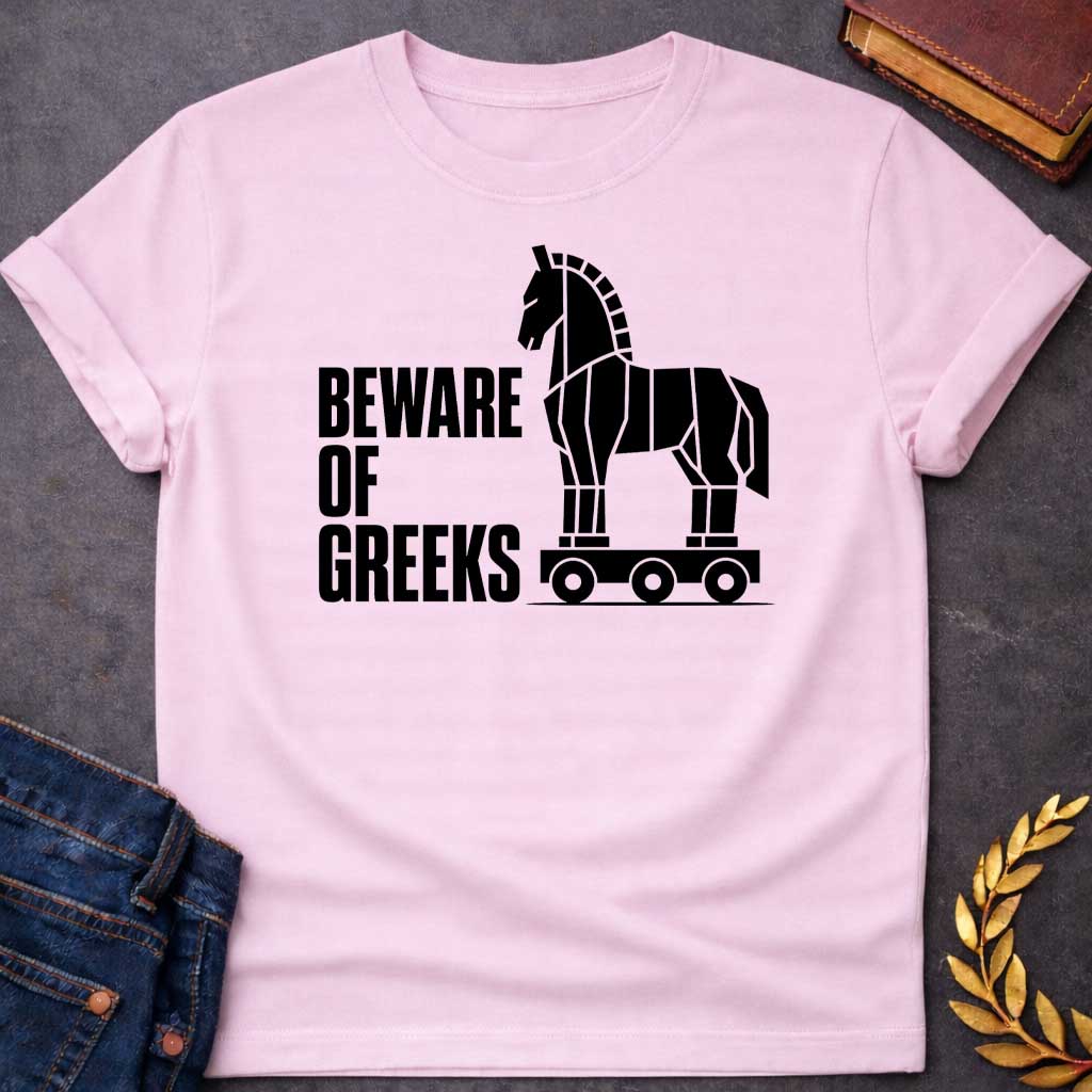 Light Pink T-shirt with a graphic in white featuring bold condensed sans-serif text reading "Beware of Greeks" alongside a flat geometric white silhouette illustration of the Trojan Horse mounted on a wheeled platform — a humorous reference to the Greek legend of the Trojan War