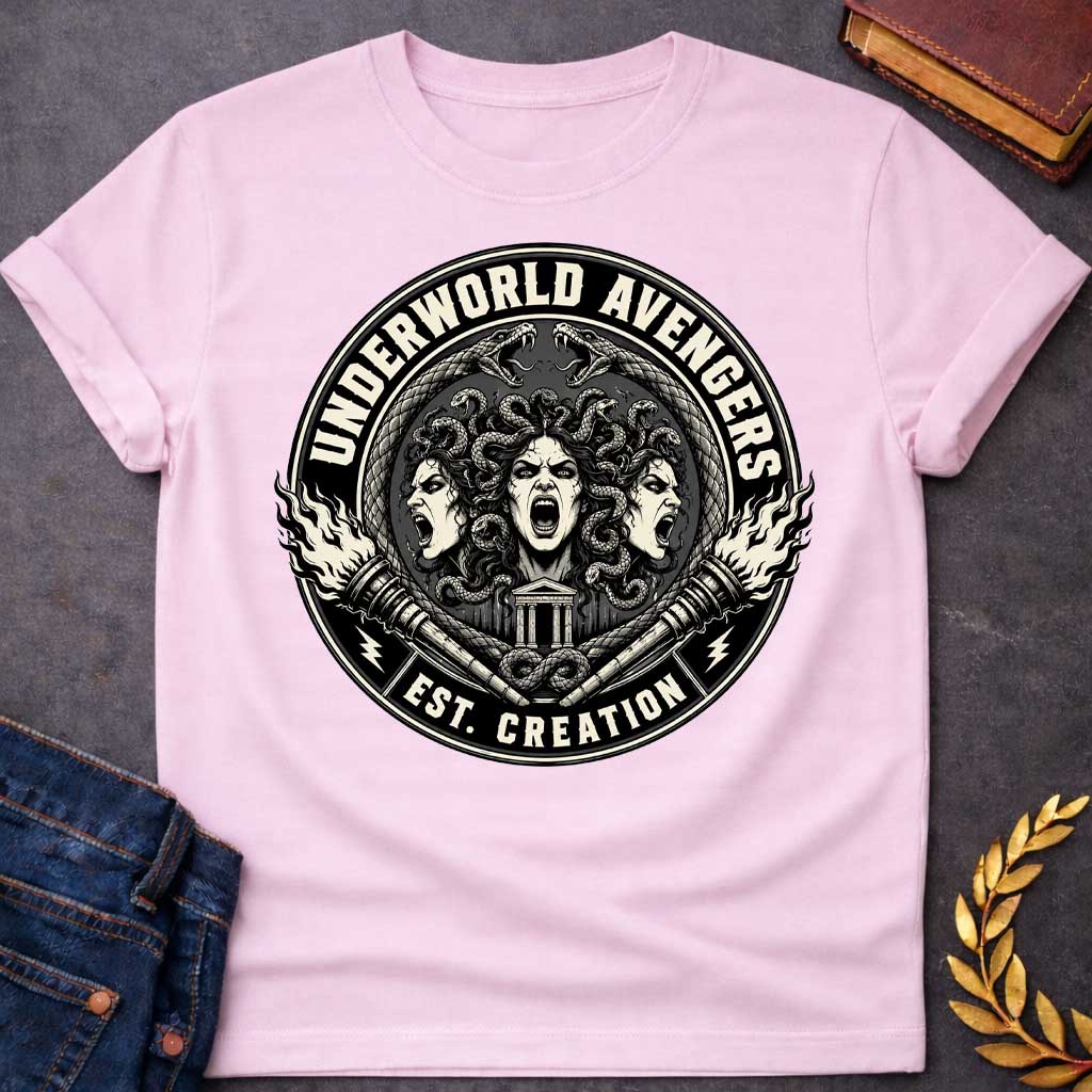 Light Pink T-shirt with an Official emblem design for the 'Underworld Avengers,' a parody combining Greek mythology with Marvel. Three Fury faces with detailed serpent hair display aggressive expressions. A Greek temple sits below, framed by crossed ornate daggers. Flames and lightning bolts accent the circular seal in vintage badge style. Text reads 'Underworld Avengers: Est. Creation.' Black and cream colors celebrate a team of divine vengeance and supernatural justice.