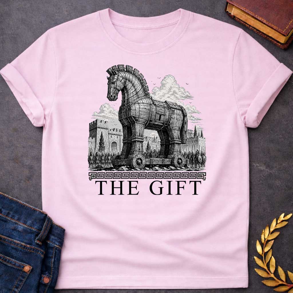 Light Pink T-shirt with a graphic in black featuring an exceptionally detailed fine-line engraving-style illustration of the Trojan Horse towering over the walls of Troy, surrounded by crowds of armored Greek soldiers with spears and shields, set against dramatic billowing clouds. A Greek meander border separates the scene from large bold classical serif text below reading "The Gift" — an ironic reference to the Greek legend of the Trojan War