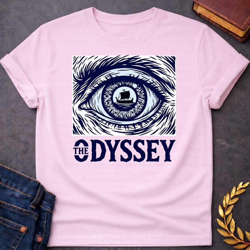 Light Pink T-Shirt with a dramatic graphic design for 'The Odyssey' featuring a stylized eye in navy blue and white. The iris contains a silhouette of an ancient Greek ship with a single sail, surrounded by radiating lines suggesting both an iris pattern and oceanic waves. Swirling, turbulent linework evokes stormy seas and Odysseus's tumultuous journey. Bold serif text reads 'THE ODYSSEY' in navy blue. Combines classical maritime imagery with modern design, emphasizing vision, journey, destiny, and fate.
