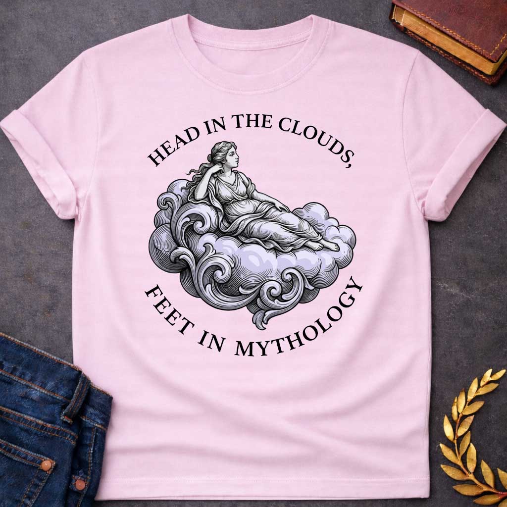 Light Pink T-shirt with a classical Greek mythology t-shirt design featuring a detailed engraving-style illustration. A woman in a traditional draped chiton relaxes gracefully, reclining on a large, swirling baroque-style cloud shaded in a pale purple hue. Arched above her is the text "HEAD IN THE CLOUDS," and curved inversely below the cloud is "FEET IN MYTHOLOGY," all written in a clean black serif font.