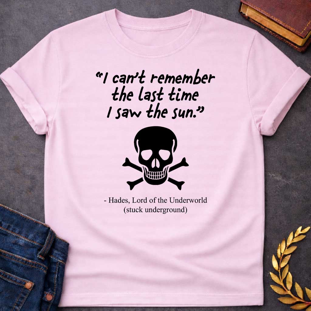 Light Pink T-shirt graphic in black and white featuring a handwritten-style quote reading "I can't remember the last time I saw the sun." above a classic skull and crossbones illustration, with the humorous attribution below reading "- Hades, Lord of the Underworld (stuck underground)