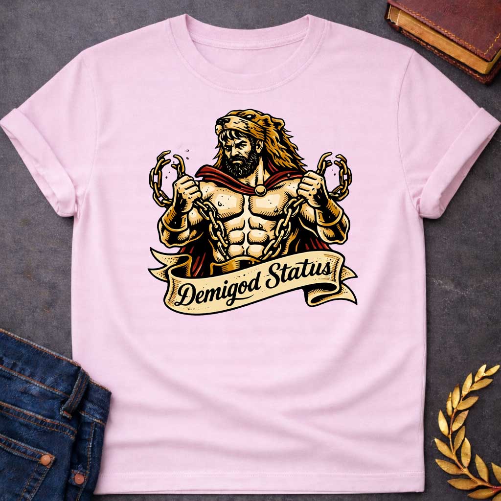 Light Pink T-shirt featuring a muscular, bearded figure resembling Heracles, wearing a lion-skin hood and a red cape, as he heroically snaps thick golden chains with his hands. Below the illustration is a flowing, decorative banner with the text "Demigod Status" written in a stylish script font,