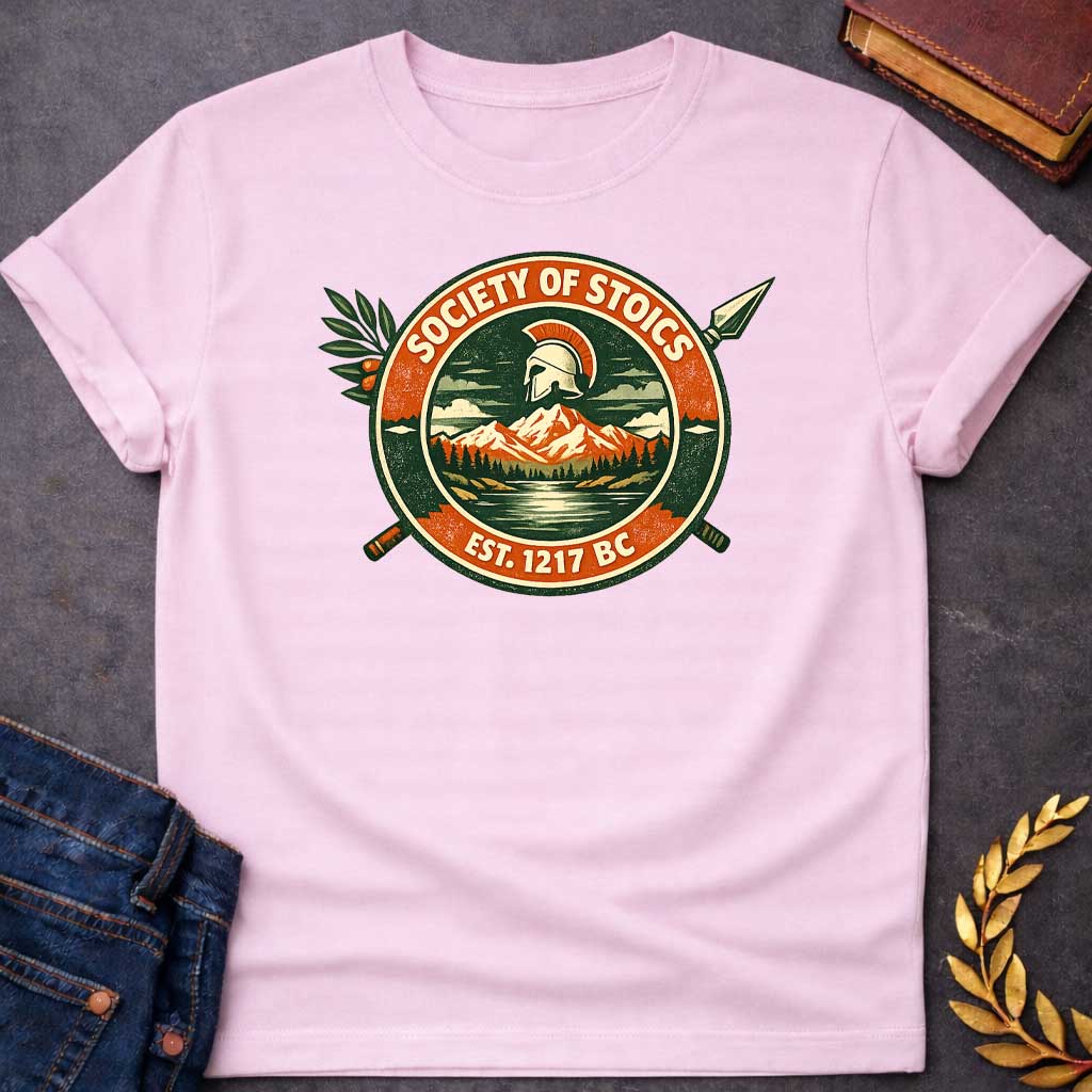 Light Pink T-shirt graphic featuring a circular vintage badge design with the text "Society of Stoics" arched above and "Est. 1217 BC" below. The center illustration shows a Spartan helmet floating above a mountain landscape with pine trees and a reflective lake, rendered in dark green, orange, and cream tones. Two crossed spears extend behind the badge, with an olive branch decorating the upper left