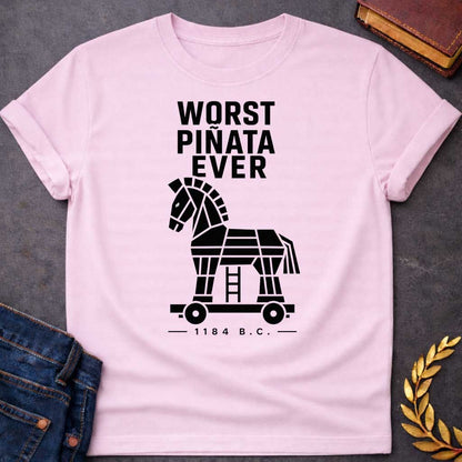 Light Pink T-shirt with a graphic in white featuring bold condensed sans-serif text reading "Worst Piñata Ever" above a detailed flat geometric white silhouette illustration of the Trojan Horse on a wheeled platform with a visible ladder underneath, with a small datestamp below reading "— 1184 B.C. —" — a humorous reference to the Greek legend of the Trojan War